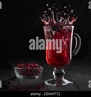 Roter Beeren-Tee mit elegantem Spritzer und Wirbel in Glas Weinglas mit reifen Preiselbeere, Heidelbeere auf schwarzem Holztisch im dunkelschwarzen Innenraum, quadratisch. Stockfoto