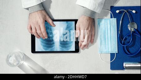 Professioneller Arzt an seinem Schreibtisch: Er überprüft das Röntgenbild der Lunge eines Patienten auf einem digitalen Tablet Stockfoto