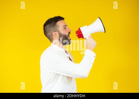 Mann schreit in ein Megaphon über gelbem Hintergrund. Stockfoto