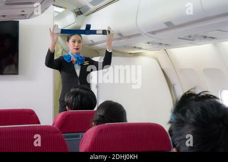 Die Asian Air Hostess-Mitarbeiter der Fluggesellschaft führen den Passagieren vor dem Abflug im Kabinenflugzeug Sicherheitsverfahren zum Anschnallen des Sicherheitsgurts vor. Stockfoto