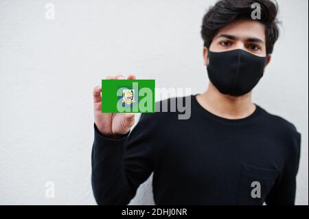 Indonesian Mann tragen ganz schwarz mit Gesichtsmaske halten Bengkulu Flagge in der Hand isoliert auf weißem Hintergrund. Provinzen Indonesiens Coronavirus Konzept. Stockfoto