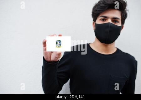 Indonesian Mann tragen ganz schwarz mit Gesichtsmaske halten Riau-Inseln Flagge in der Hand isoliert auf weißem Hintergrund. Provinzen Indonesiens Coronavirus Konzept. Stockfoto