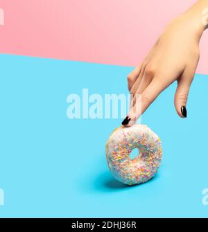 Womans Hand hält bunte Donut auf blauem Hintergrund. Modell Vorlage für Bäckerei Stockfoto
