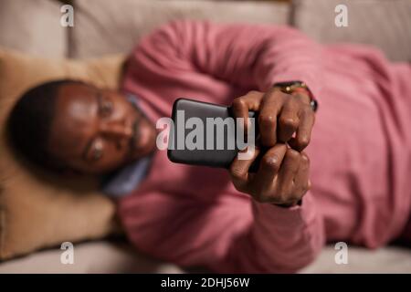 High-Angle-Ansicht der afrikanischen Mann tippen auf Handy Online arbeiten, während Sie auf dem Sofa liegen Stockfoto