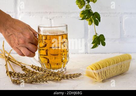 Glas Becher Bier in der Hand einer Frau mit Kartoffelchips, Ohren von Gerste und einem Hopfenzweig auf dem weißen Hintergrund. Stockfoto