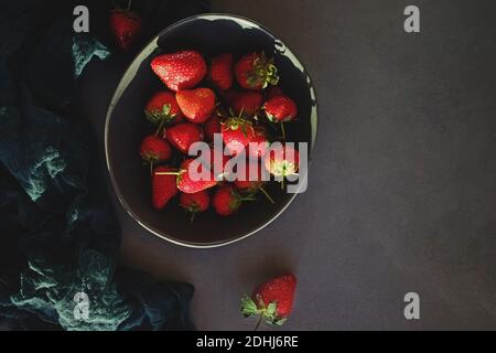 Frische Bio-Erdbeeren in einer Schüssel auf einem Steintisch, Draufsicht. Dunkle und stimmungsvolle Fotos, Low-Key. Stockfoto