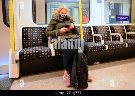 London, England, Großbritannien. Frau in einem U-Bahn-Zug, die ihr Handy benutzt und eine Gesichtsmaske während der COVID-Pandemie trug, Dezember 2020 Stockfoto