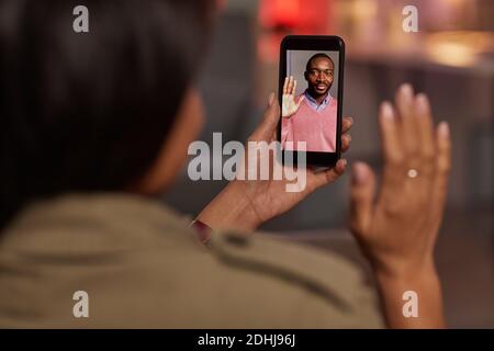 Junge Frau hält Handy und winkt zu ihrem Freund Während Sie mit ihm online sprechen Stockfoto