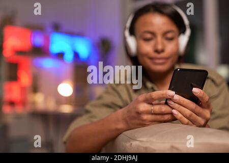 Junge Frau in Kopfhörern tippt Nachricht auf ihr Handy Während Sie auf dem Sofa sitzen Stockfoto