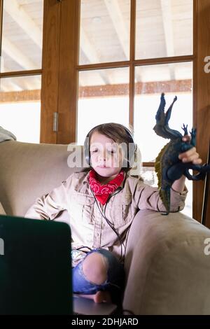 Kleiner Junge im Safari-Outfit und Kopfhörer, der einen Film ansieht Auf einem Laptop Stockfoto