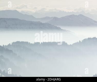 Schnee Berge im niedrig liegenden Inversion Tal Nebel. Silhouetten von nebligen Bergen und Bäumen. Landschaftlich schöne verschneite Winterlandschaft. Blick von Stuiben Swiss Stockfoto