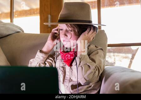 Kleiner Junge im Safari-Outfit und Kopfhörer, der einen Film ansieht Auf einem Laptop Stockfoto