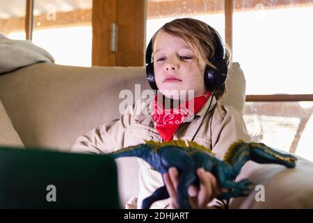 Kleiner Junge im Safari-Outfit und Kopfhörer, der einen Film ansieht Auf einem Laptop Stockfoto