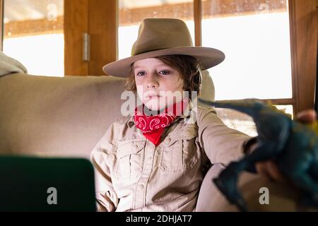 Kleiner Junge im Safari-Outfit und Kopfhörer, der einen Film ansieht Auf einem Laptop Stockfoto