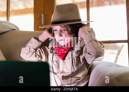 Kleiner Junge im Safari-Outfit und Kopfhörer, der einen Film ansieht Auf einem Laptop Stockfoto