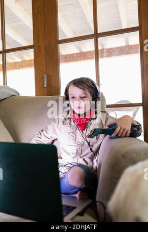 Kleiner Junge im Safari-Outfit und Kopfhörer, der einen Film ansieht Auf einem Laptop Stockfoto