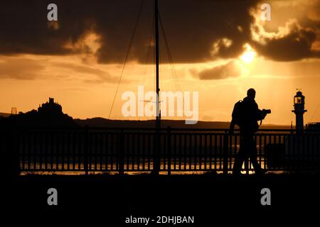 Ein Fotograf fängt die Ruhe vor Storm Alex ein, wenn die Sonne hinter dem Leuchtturm am Hafen von Penzance am ersten Oktobertag aufgeht. Stockfoto