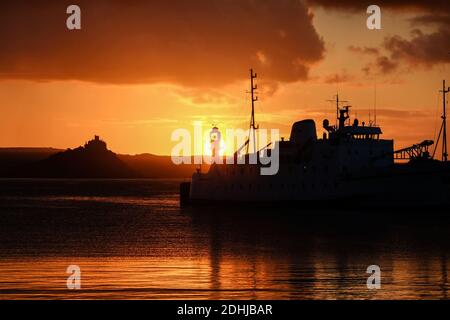 Die Ruhe vor Storm Alex, wenn die Sonne hinter dem Penzance Harbour Leuchtturm am ersten Oktobertag aufgeht. Stockfoto