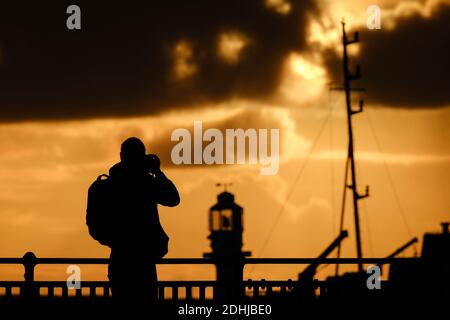 Ein Fotograf fängt die Ruhe vor Storm Alex ein, wenn die Sonne hinter dem Leuchtturm am Hafen von Penzance am ersten Oktobertag aufgeht. Stockfoto