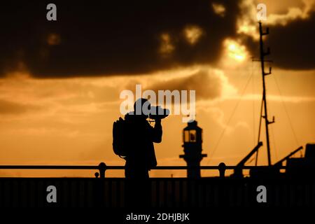 Ein Fotograf fängt die Ruhe vor Storm Alex ein, wenn die Sonne hinter dem Leuchtturm am Hafen von Penzance am ersten Oktobertag aufgeht. Stockfoto