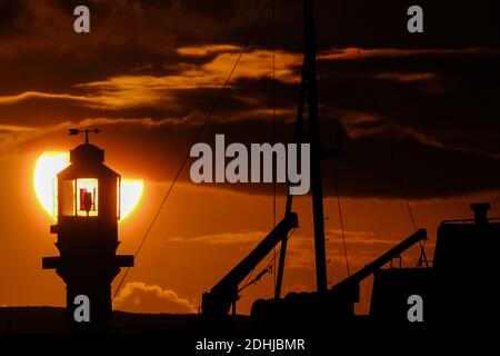 Die Ruhe vor Storm Alex, wenn die Sonne hinter dem Penzance Harbour Leuchtturm am ersten Oktobertag aufgeht. Stockfoto