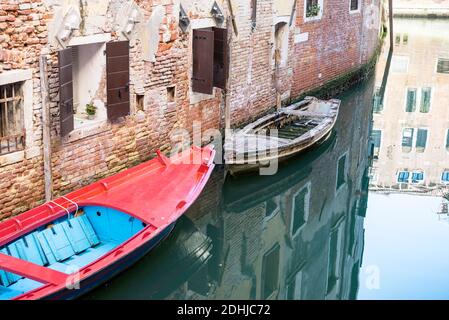 Ein altes Boot, das repariert werden muss, neben einem Leuchtend rotes Boot in Venedig Italien Stockfoto