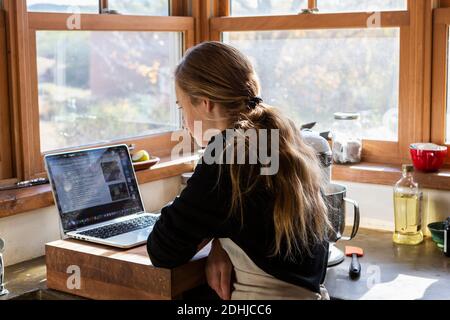 Teenager-Mädchen in einer Küche nach einem Backrezept auf einem Laptop. Stockfoto