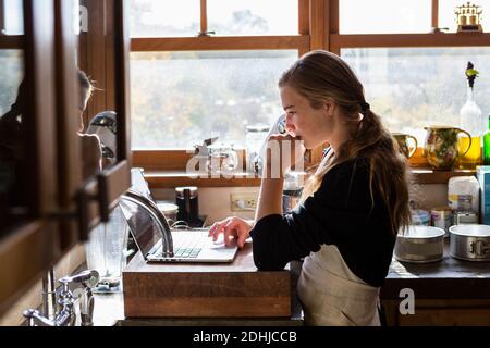 Teenager-Mädchen in einer Küche nach einem Backrezept auf einem Laptop. Stockfoto