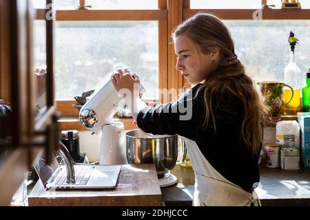 Teenager-Mädchen in einer Küche nach einem Backrezept auf einem Laptop. Stockfoto