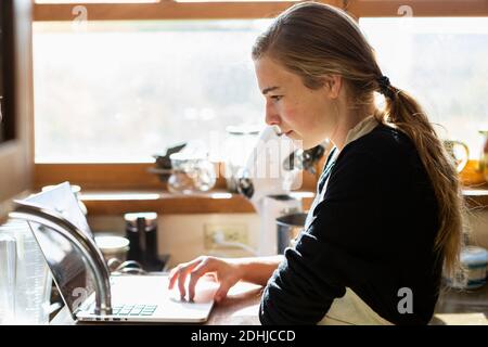 Teenager-Mädchen in einer Küche nach einem Backrezept auf einem Laptop. Stockfoto