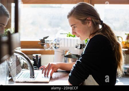 Teenager-Mädchen in einer Küche nach einem Backrezept auf einem Laptop. Stockfoto