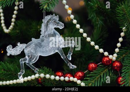 Spielzeug Pferd auf einem Weihnachtsbaum auf einem grünen Hintergrund mit Lichtern und roten und weißen Perlen. Nahaufnahme von Weihnachtsbaumschmuck. Stockfoto