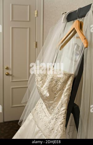 Hochzeitskleid und Schleier hängen auf dem Regal im Hotelzimmer. Stockfoto