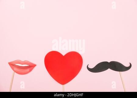 Valentinstag, Liebe, romantisches Konzept. Rotes Herz, Schnurrbärte und Lippen Papierstütze auf rosa Hintergrund. Grußkarte. Flach liegend, Draufsicht, Kopierbereich. Stockfoto