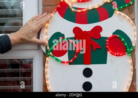 Nahaufnahme von mans Hand Aufstellen inländischen Weihnachtsbeleuchtung für die Weihnachtszeit. Schrauben Schneemann Licht Funktion zur Hauswand im Winter draußen Stockfoto