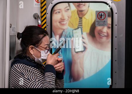 Eine Pendlerin telefoniert, als sie mit der MTR-U-Bahn in Hongkong fährt.Hongkong erlebt derzeit eine Welle von vier Covid-19-Fällen, während die Regierung für die nächsten Wochen neue soziale Einschränkungen und Regeln in Restaurants, Schönheitssalons, Bars und Fitnessstudios eingeführt hat. Stockfoto