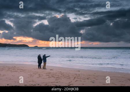 Ein paar Urlauber genießen einen spektakulären Sonnenuntergang über der Fistral Bay in Newquay in Cornwall. Stockfoto