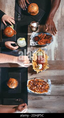 Von oben der Ernte multirassische Gruppe von Freunden sitzen an Tisch mit verschiedenen Junk-Food und genießen Zeitvertreib zusammen Stockfoto