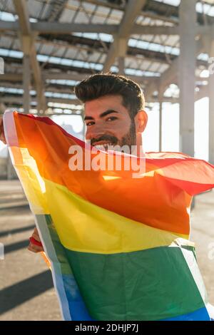 Junge erfreut Gay Männlich stehen in der Straße mit Regenbogenfahne Und Blick auf die Kamera Stockfoto