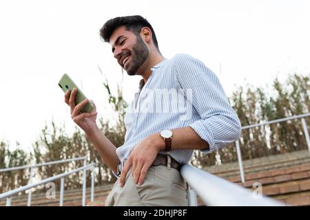 Von unten von Inhalten männlichen Lesestoff Nachrichten in sozialen Medien Während ich mich in der Stadt auf das Geländer auf der Treppe lehnte und lächelte Stockfoto