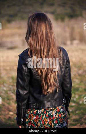 Rückansicht von unkenntlich Weibchen in Lederjacke und mit Lange wellige Haare stehen auf der Wiese Stockfoto