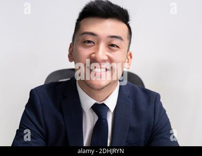Positive junge asiatische männliche Executive Manager in Business-Stil tragen Blick auf die Kamera, während Sie im Büro sitzen Stockfoto