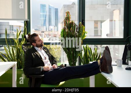 Seitenansicht des müden jungen Geschäftsmannes in formellem Anzug mit Augen geschlossen Denken über erfolgreiche Geschäftsstrategie in modernen Arbeitsbereichen Stockfoto