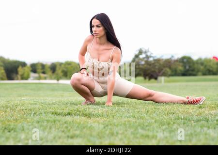 Voller Körper von selbstbewusst bestimmt junge fit weiblich in stilvoll activewear und Sneakers machen Stretching-Übungen auf grünem Rasen Während des Fitnessstudios w Stockfoto