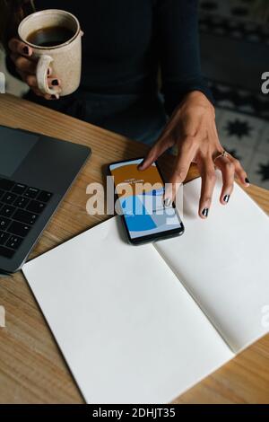 Von oben der Ernte anonyme Frau, die am Tisch mit sitzt tasse Kaffee und Analyse Diagramm auf dem Smartphone während der Arbeit Online-Projekt Stockfoto