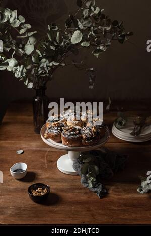 Hoher Winkel von köstlichen hausgemachten süßen Brötchen mit Mohn Samen serviert auf Stand in der Nähe von Vase mit frischem Grün platziert Pflanzen auf Holztisch Stockfoto