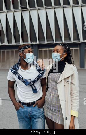Positive junge afroamerikanische Mann und Frau in trendigen Casual Outfits und Schutzmasken für Coronavirus Prävention Spaß haben und umarmen während sp Stockfoto