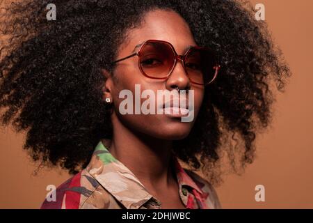 Selbstbewusste kubanische Frau mit Afro-Frisur, Sonnenbrille mit geblümtem Hemd und Blick auf die Kamera Stockfoto