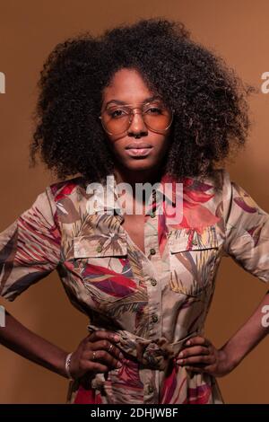 Selbstbewusste kubanische Frau mit Afro-Frisur, Sonnenbrille mit geblümtem Hemd und Blick auf die Kamera Stockfoto