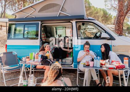 Gruppe weiblicher Freunde, die sich in der Nähe eines geparkten Transporters in Wäldern treffen Und Chillen an sonnigen Tag während der Sommerreise Stockfoto